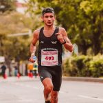 Focused male athlete running in a marathon, wearing a tank top and holding a bottle of water.
